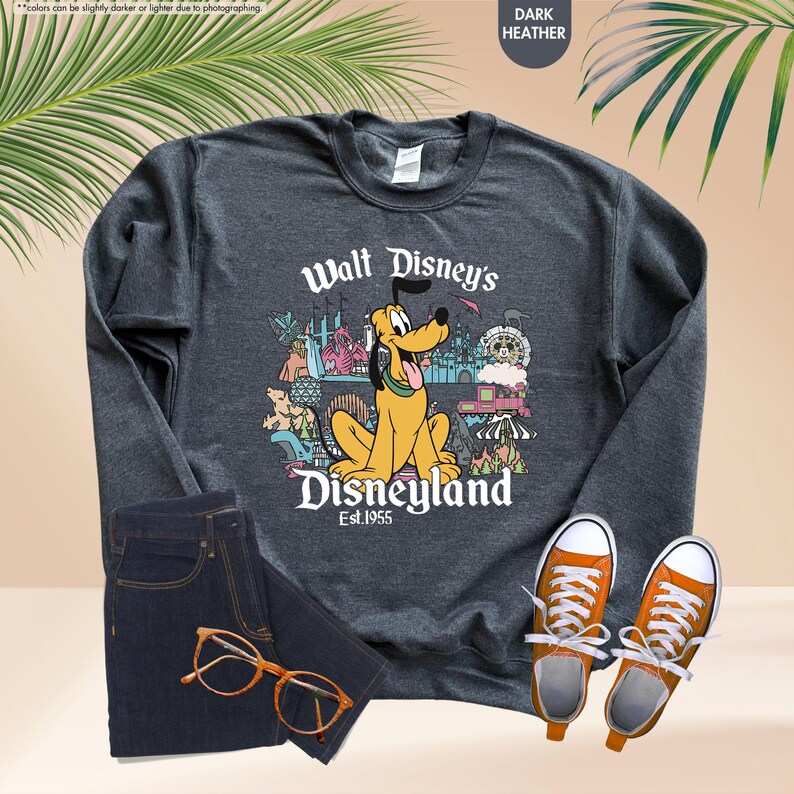 May include: Dark heather gray sweatshirt featuring a graphic of Pluto from Walt Disney's Disneyland. The design includes the text "Walt Disney's Disneyland Est. 1955" and various park icons. The sweatshirt is paired with dark blue jeans and orange sneakers.
