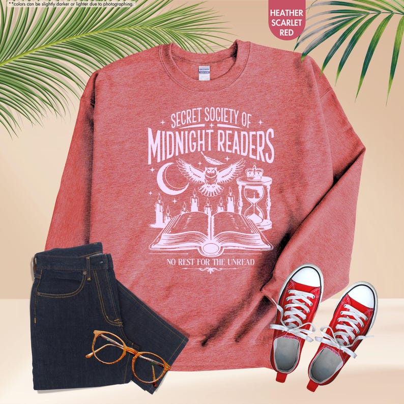 May include: Heather scarlet red sweatshirt with the text "SECRET SOCIETY OF MIDNIGHT READERS" and a graphic of an owl, book, and candles. The image also includes dark blue jeans, red sneakers, and eyeglasses.