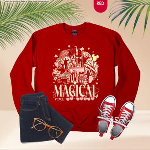 May include: A red sweatshirt with a graphic that says "The Most Magical Place" with a castle and other illustrations. The image also shows a pair of blue jeans, red sneakers, and gold-rimmed glasses.