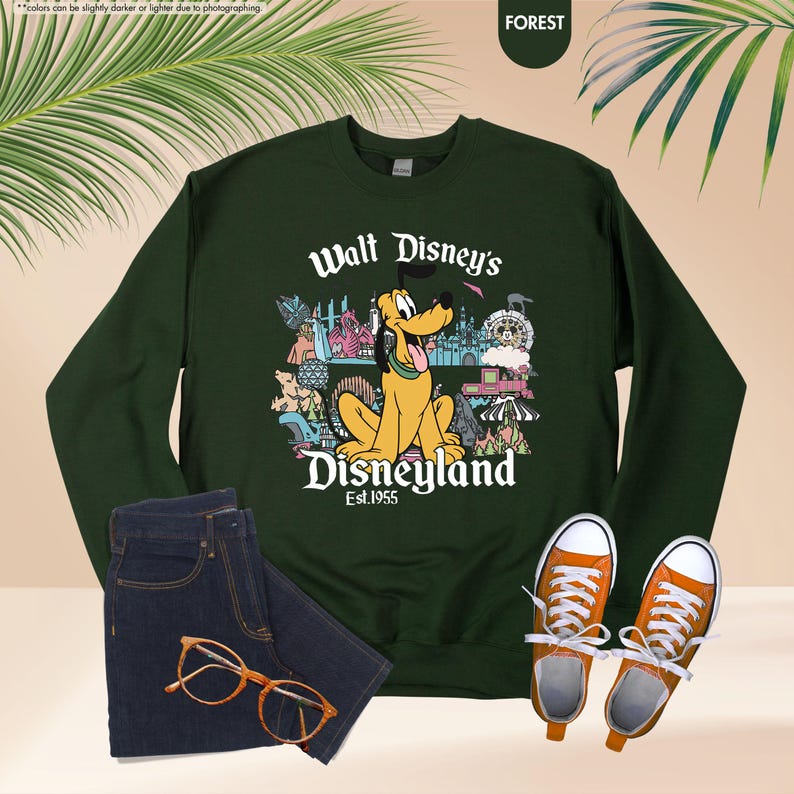 May include: A dark green sweatshirt featuring Pluto from Disney's Disneyland, with the text "Walt Disney's Disneyland Est. 1955". The image also shows a pair of blue jeans, orange-colored glasses, and orange sneakers.