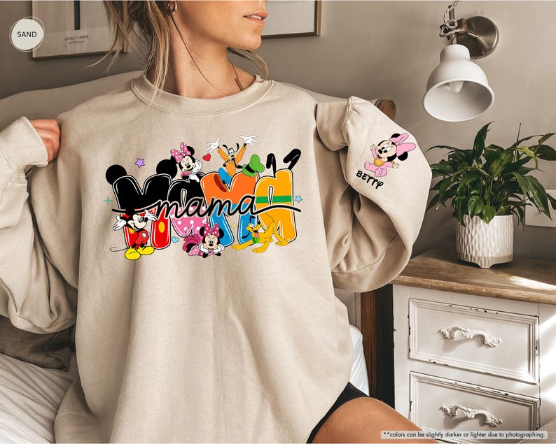 K&ouml;nnte beinhalten: Beiges Sweatshirt mit dem Wort "Mama" in bunten Blockbuchstaben, mit den Disney-Figuren Mickey Mouse, Minnie Mouse, Goofy und Pluto. Der &Auml;rmel hat eine Minnie Mouse Grafik und den Namen "Betty".