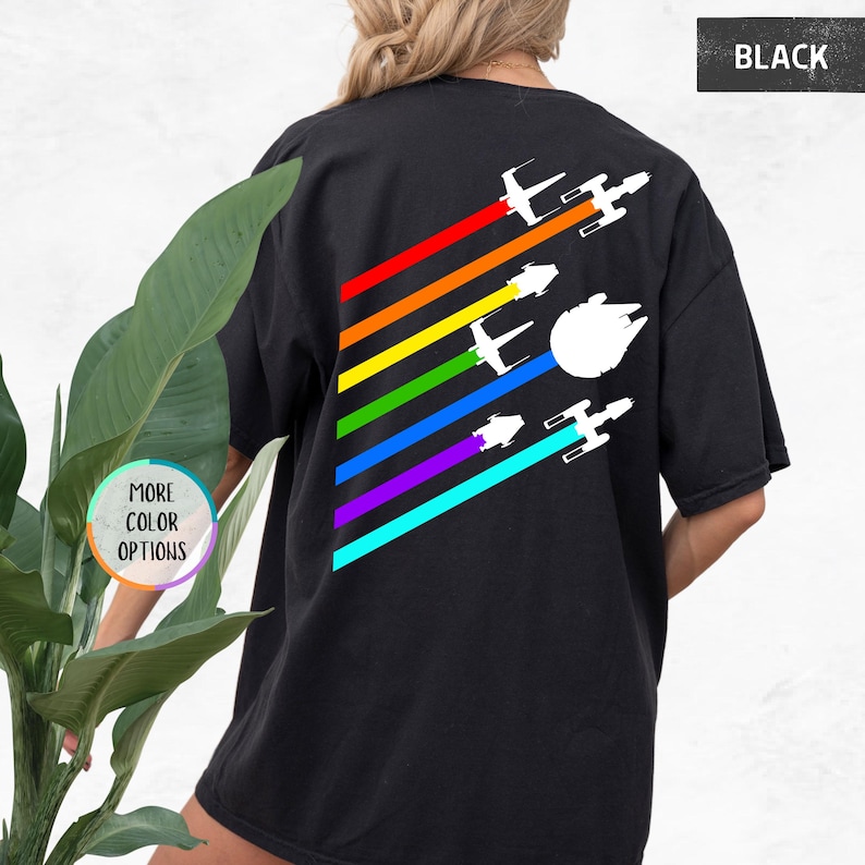 K&ouml;nnte beinhalten: Schwarzes T-Shirt mit einem Regenbogenstreifen-Design und wei&szlig;en Silhouetten von Star Wars-Raumschiffen, die &uuml;ber die Streifen fliegen. Der Text "BLACK" befindet sich in der oberen rechten Ecke des Bildes.
