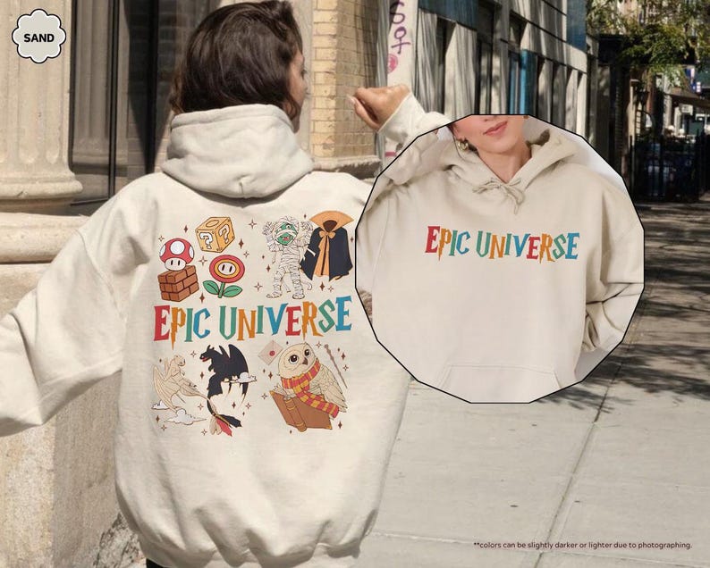May include: Sand-colored hoodie with the text "EPIC UNIVERSE" in colorful letters. The back of the hoodie features various cartoon graphics, including a mushroom, a question mark block, and a mummy. The hoodie has a drawstring hood.