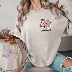 May include: A sand colored sweatshirt with a graphic of Mickey Mouse and Donald Duck on the front. The text "Danielle" is below the graphic. The back of the sweatshirt has a graphic of Mickey Mouse and the text "Disney with my bestie".