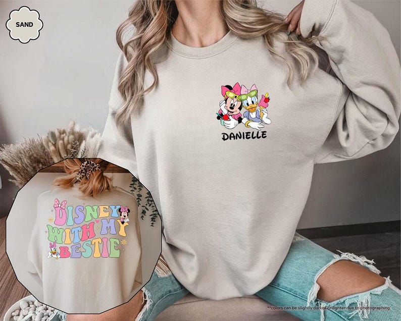 May include: A sand colored sweatshirt with a graphic of Mickey Mouse and Donald Duck on the front. The text "Danielle" is below the graphic. The back of the sweatshirt has a graphic of Mickey Mouse and the text "Disney with my bestie".