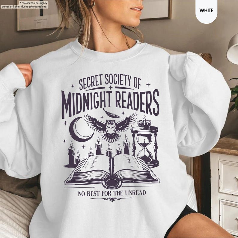 May include: White sweatshirt with a graphic design featuring the text "SECRET SOCIETY OF MIDNIGHT READERS". The design includes an owl, moon, candles, an hourglass, and an open book. The phrase "NO REST FOR THE UNREAD" is also present.