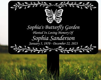 May include: Black metal garden sign with white butterfly and floral design. The sign reads "Sophia's Butterfly Garden Planted In Loving Memory Of Sophia Sanderson January 5, 1970 - December 22, 2023".