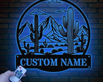 May include: A black metal silhouette of a desert landscape with cacti and mountains. The silhouette is illuminated from behind, creating a glowing effect. The text "CUSTOM NAME" is displayed on a separate plaque below the silhouette.