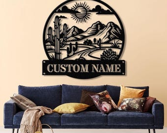 May include: Black metal wall art featuring a desert landscape with a cactus, mountains, and a winding road. The art includes a personalized nameplate that reads "CUSTOM NAME".