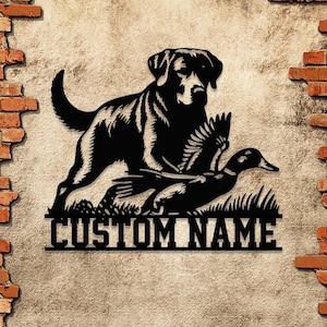 May include: Black metal silhouette of a Labrador Retriever dog pointing at a flying duck with the text "CUSTOM NAME" below.