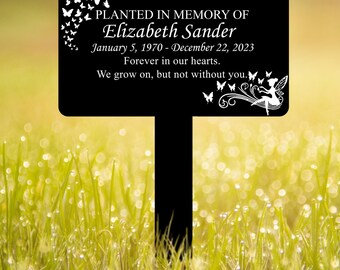 May include: A black memorial garden stake with white text and butterfly graphics. The text reads "PLANTED IN MEMORY OF Elizabeth Sander January 5, 1970 - December 22, 2023 Forever in our hearts. We grow on, but not without you."