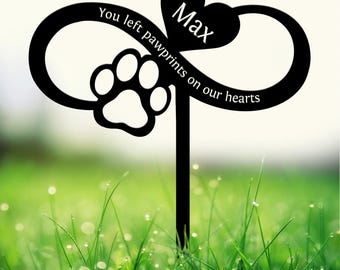 May include: Black metal garden stake with an infinity symbol, paw print, and heart with the name "Max." The text reads "You left pawprints on our hearts." The stake is in a green grassy area.