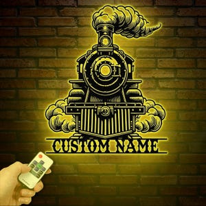 May include: A yellow illuminated silhouette of a vintage steam locomotive with smoke billowing from the chimney. The locomotive is on a brick wall background. The text "CUSTOM NAME" is below the locomotive.