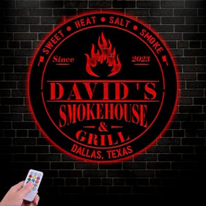 May include: A black and red round sign with the text "Sweet Heat Salt Smoke" around the edge. The center of the sign has a red flame design and the text "David's Smokehouse & Grill Dallas, Texas" with the year "2023" and the word "Since" above the text.
