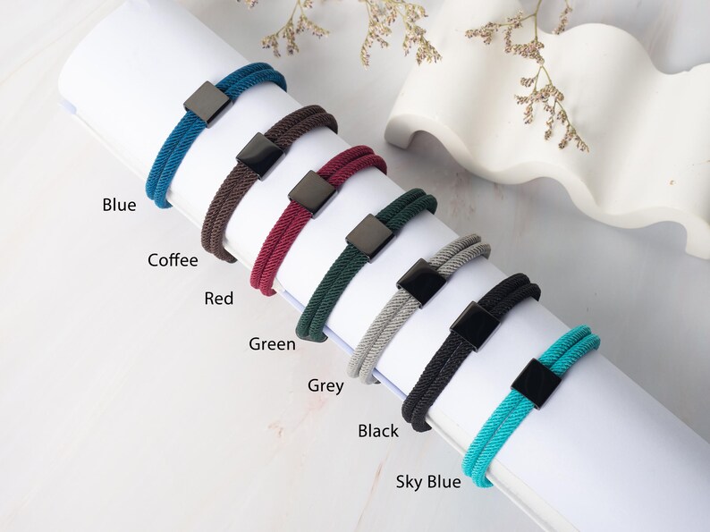 May include: A selection of colorful bracelets in blue, coffee, red, green, grey, black, and sky blue. Each bracelet features a woven cord design and a square, dark-colored clasp. The colors are labeled on the image.