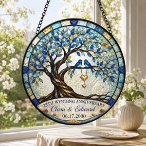 May include: A circular stained glass suncatcher featuring a tree with blue and gold leaves, two blue birds perched on a branch, and two hanging gold hearts. The text reads 25TH WEDDING ANNIVERSARY, Clara & Edward, and 06.17.2000.