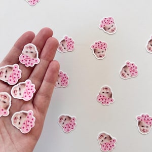 Op de afbeelding: Een witte achtergrond met roze en witte confetti met daarop een babygezicht met een roze cowboyhoed met roze sterren.