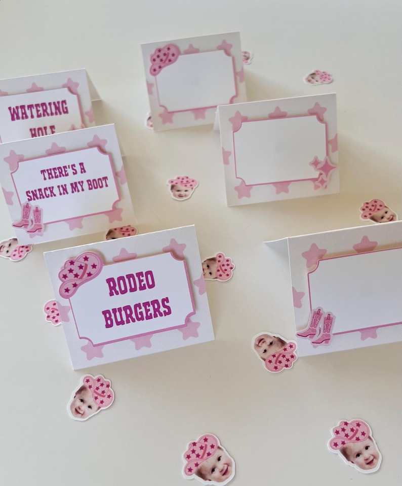 Op de afbeelding: Roze en witte tafelkaarten met een roze ster- en cowboyhoedontwerp. De kaarten hebben de tekst "Watering Hole", "There's a Snack in My Boot" en "Rodeo Burgers".