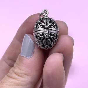 Peut inclure: Un charme en argent filigrané en forme d'œuf avec une ouverture à charnière. Le charme a un délicat motif floral.