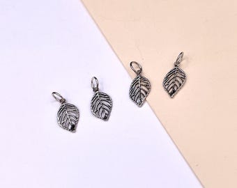 May include: Four silver leaf charms with a delicate, intricate design. The charms are perfect for adding a touch of nature to jewelry projects.