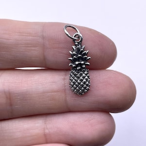 May include: A silver pineapple charm with a detailed design. The charm is ideal for adding a tropical touch to jewellery.