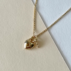 May include: A gold-colored necklace featuring a heart-shaped pendant with a key charm. The pendant and key are suspended from a delicate chain. The necklace is displayed on a neutral background.