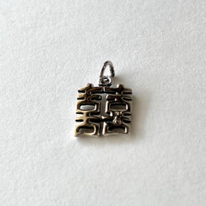 May include: Silver charm with a Chinese double happiness symbol, a traditional symbol of good fortune and happiness in Chinese culture.