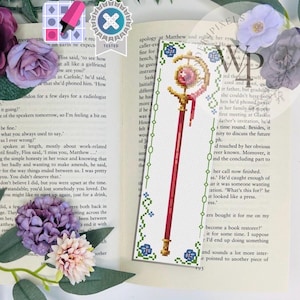 Peut inclure: Marque-page rouge et or avec un motif au point de croix. Le marque-page présente un bâton avec un croissant de lune rose et un motif d'étoile en haut, et est décoré d'éléments floraux.