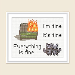 May include: Cross-stitch art framed in white. The design features a dumpster on fire, two raccoons, and the text "I'm fine, It's fine, Everything is fine" in black block letters. The dumpster is green and brown, and the flames are orange.