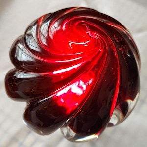 May include: A clear glass object with a spiral design. The object is primarily red with dark red and clear accents. The spiral pattern creates a swirling effect, and the glass appears to be smooth and polished.