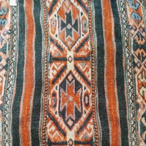 May include: A close-up of a woven fabric with a repeating geometric pattern in shades of orange, black, white, and blue.