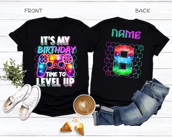 May include: Black t-shirts with birthday graphics. The front shirt says "IT'S MY BIRTHDAY TIME TO LEVEL UP" with a colorful video game controller. The back shirt has the word "NAME" and a number 8 in a hexagon pattern.