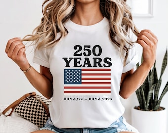 May include: White t-shirt with the text "250 YEARS" above an American flag graphic. The flag has red and white stripes and a blue field with white stars. The text "JULY 4, 1776 - JULY 4, 2026" is below the flag.