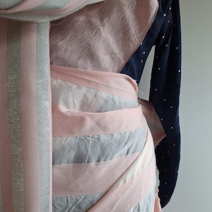Pode incluir: Um tecido listrado rosa e cinza com uma superfície texturizada. O tecido está dobrado e drapeado, mostrando as diferentes cores e padrões.