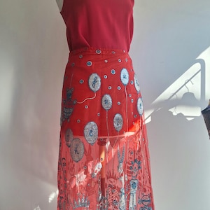 May include: A red sleeveless top and a sheer red skirt with silver and blue embellishments. The skirt features a whimsical design of balloons and cartoon characters. The outfit is displayed on a mannequin.