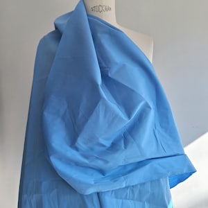 Pode incluir: Um tecido azul claro drapeado sobre um manequim. O tecido é liso e tem um leve brilho.