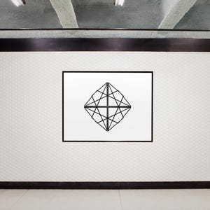 May include: A black and white geometric design in a square frame on a white tiled wall.