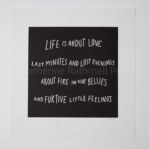 May include: A monochrome print featuring the words "LIFE IS ABOUT LOVE" and other phrases in a handwritten font. The print is set against a black square on a white background.