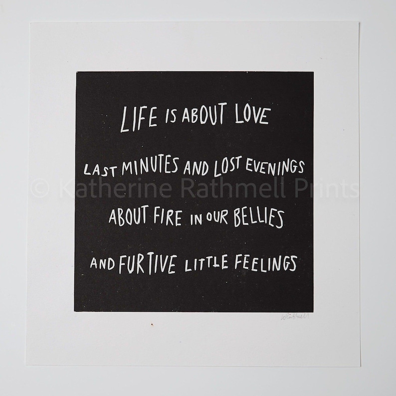 May include: A monochrome print featuring the words "LIFE IS ABOUT LOVE" and other phrases in a handwritten font. The print is set against a black square on a white background.