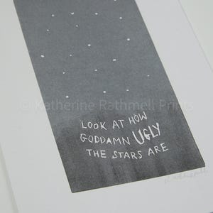 May include: A grayscale print featuring a dark gray rectangle with white dots resembling stars. The text "LOOK AT HOW GODDAMN UGLY THE STARS ARE" is written in white. The print is on white paper.