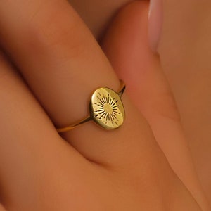 May include: A gold ring with a round, textured design featuring a sunburst pattern.