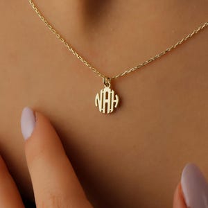 May include: A gold necklace with a circular pendant featuring the monogram "NAH".