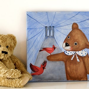May include: A plush teddy bear sits next to a square painting. The painting depicts a brown bear with a blue and white polka-dot collar, pointing at two red cardinals. The background features a blue sky and a bridge.