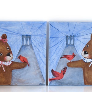 May include: Two square paintings depict brown teddy bears with red cardinals. The bears wear white collars with blue polka dots and are set against a blue background with a bridge-like structure. One bear has a pink bow.