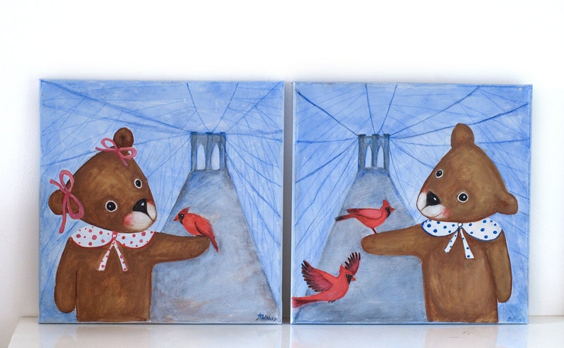 May include: Two square paintings depict brown teddy bears with red cardinals. The bears wear white collars with blue polka dots and are set against a blue background with a bridge-like structure. One bear has a pink bow.