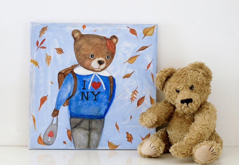 May include: A whimsical painting of a bear wearing a blue sweater with "I ❤️ NY" and a backpack, surrounded by falling leaves. A plush teddy bear sits beside the artwork. The painting is on a square canvas.