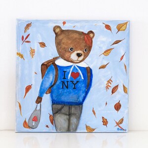 May include: An original painting of a brown bear wearing a blue sweater with "I NY" and a red heart. The bear is carrying a backpack and a bag with a mushroom design, with autumn leaves falling around it. The background is light blue.