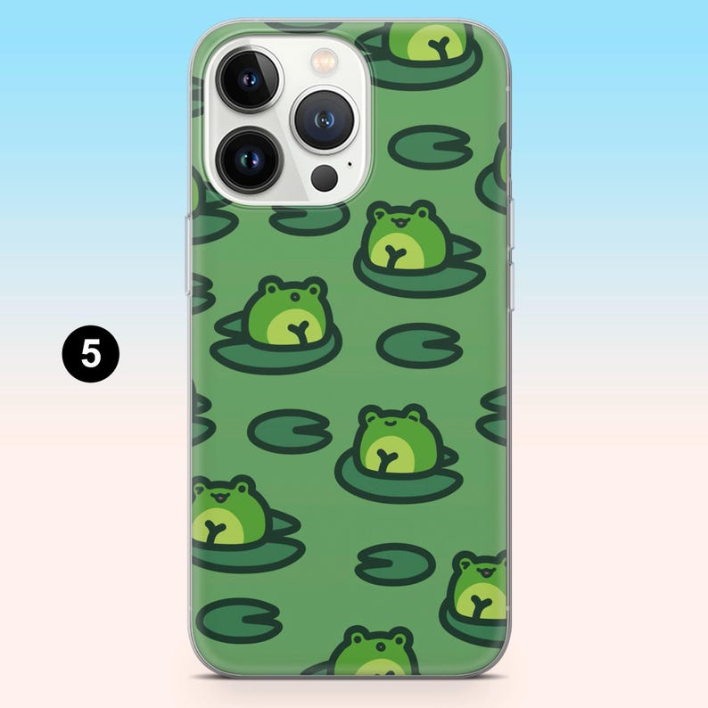 May include: Clear phone case with a green frog and lily pad pattern. The frogs are light green with yellow bellies, and the lily pads are dark green. The case has a clear border and a camera cutout.