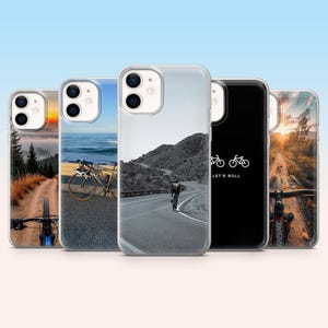 May include: A selection of phone cases with bicycle-themed imagery. The cases showcase bicycles on roads and trails, with a black case displaying the text "LET'S ROLL". The cases have a clear border, and the images feature scenic landscapes.