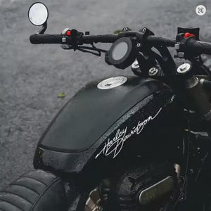 Könnte beinhalten: Schwarzes Harley Davidson Motorrad mit gebogenem Lenker, rundem Spiegel und einem Kraftstofftank mit dem Harley Davidson Logo in weißer Schrift. Das Motorrad ist nass, was darauf hindeutet, dass es regnet.